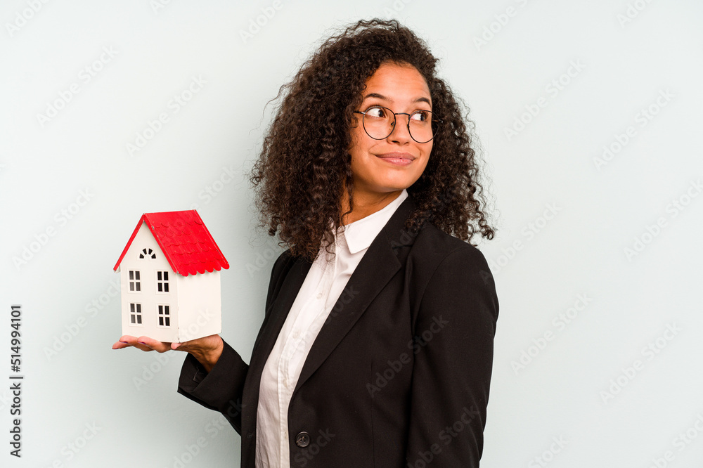 Young business Brazilian woman holding toy house isolated on white background looks aside smiling, cheerful and pleasant. Young business Brazilian woman holding toy house isolated on white background looks aside smiling, cheerful and pleasant.
