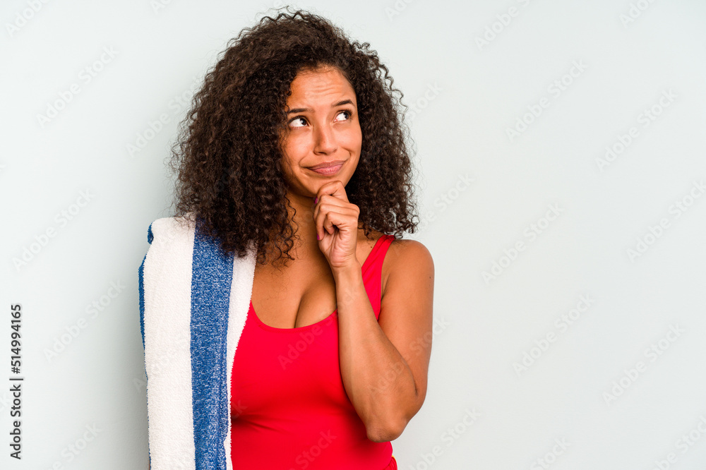 Young brazilian woman going to the beach holding a towel isolated on blue background looking sideways with doubtful and skeptical expression. Young brazilian woman going to the beach holding a towel isolated on blue background looking sideways with doubtful and skeptical expression.