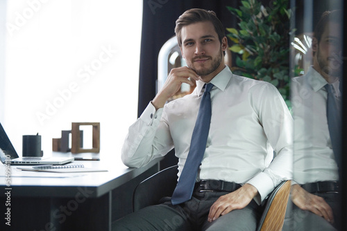 Portrait of businessman sitting in office, successful man worker employee by work desk looking at camera