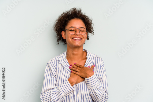 Young Brazilian woman isolated on blue background laughing keeping hands on heart, concept of happiness.