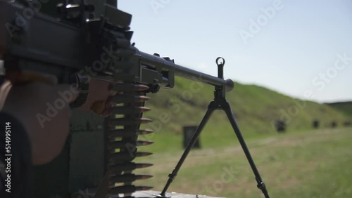 Militarian sets loaded machine gun with cartridge belt on bipod and ready to shot at shooting range photo