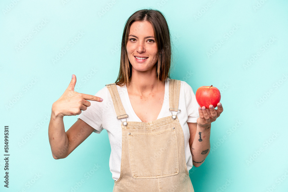 Young caucasian pregnant woman holding an apple isolated on blue background person pointing by hand to a shirt copy space, proud and confident Young caucasian pregnant woman holding an apple isolated on blue background person pointing by hand to a shirt copy space, proud and confident