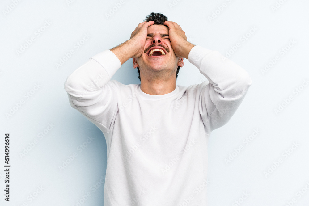Young caucasian man isolated on blue background laughs joyfully keeping hands on head. Happiness concept. Young caucasian man isolated on blue background laughs joyfully keeping hands on head. Happiness concept.