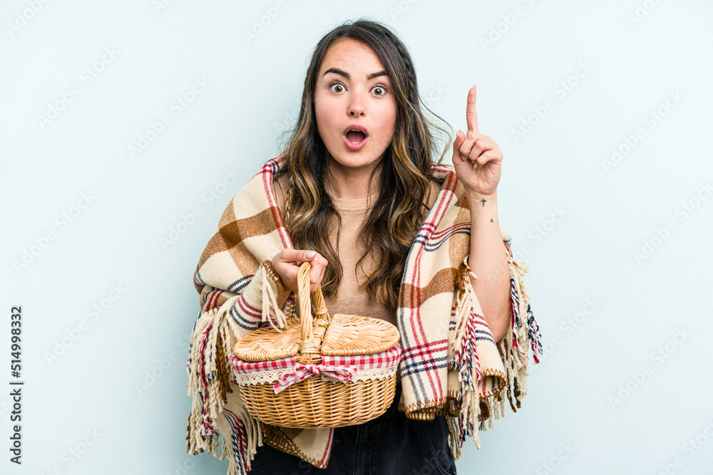 Young caucasian woman holding a picnic basket isolated on blue background having an idea, inspiration concept.