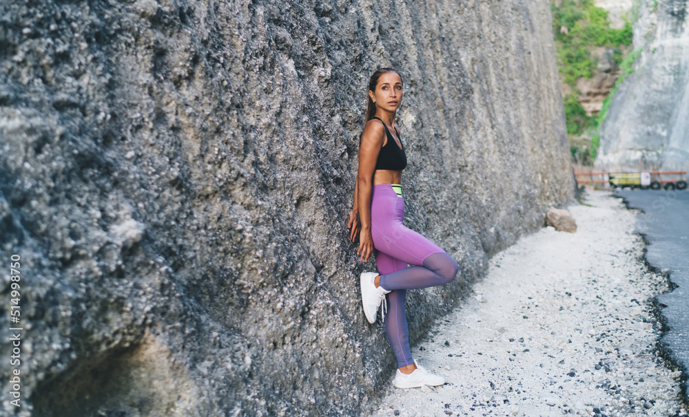 Caucasian female in activewear thinking near rock and looking away during break after cardio jogging, pensive fit girl recreating after running workout - concept of healthy lifestyle and wellness Caucasian female in activewear thinking near rock and looking away during break after cardio jogging, pensive fit girl recreating after running workout - concept of healthy lifestyle and wellness