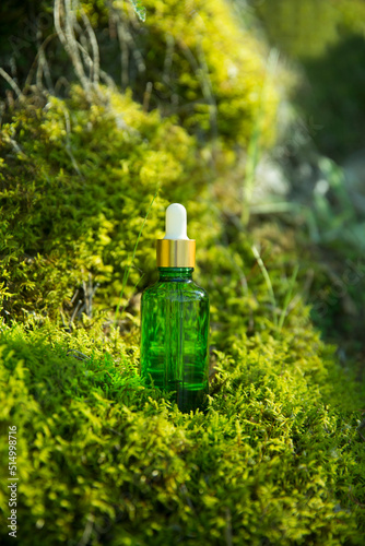 cosmetic products green glass bottl with oil on moss against a forest background photo