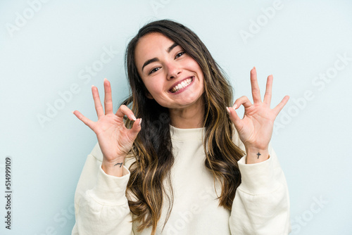 Young caucasian woman isolated on blue background cheerful and confident showing ok gesture.