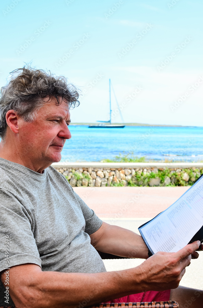 old man reading the menu of a restaurant by the Mediterranean Sea