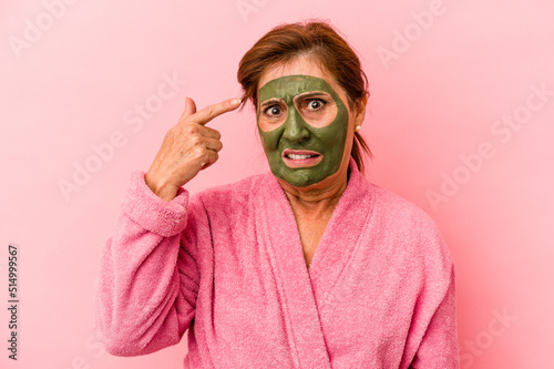 Middle age caucasian woman wearing a facial mask isolated on pink background showing a disappointment gesture with forefinger.
