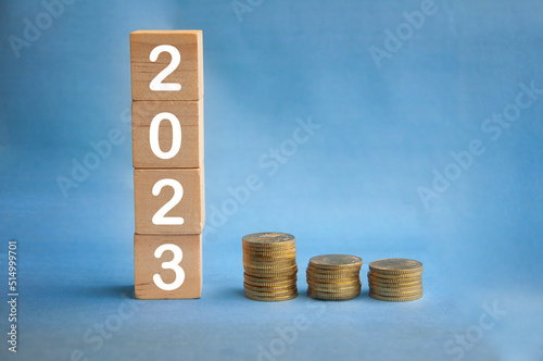New year 2023 text on wooden blocks with gold coins on blue background. New year concept and copy space