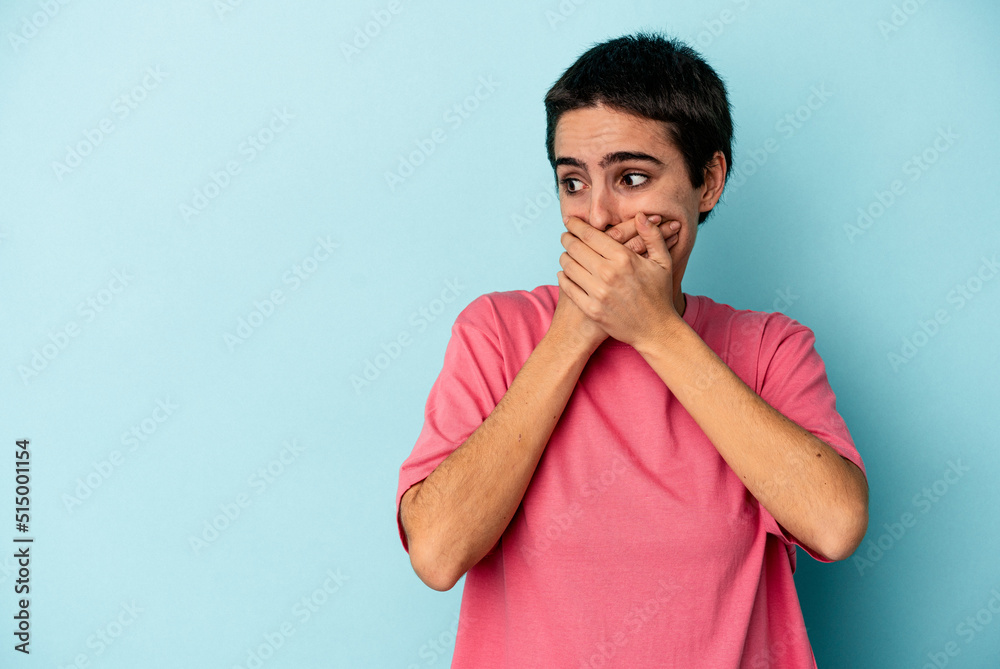 Young caucasian woman isolated on blue background thoughtful looking to a copy space covering mouth with hand. Young caucasian woman isolated on blue background thoughtful looking to a copy space covering mouth with hand.