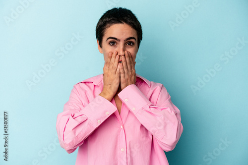 Young caucasian woman isolated on blue background shocked  covering mouth with hands  anxious to discover something new.