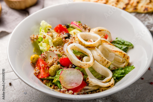 фотографія salad with squid and vegetables on white plate on white wooden table