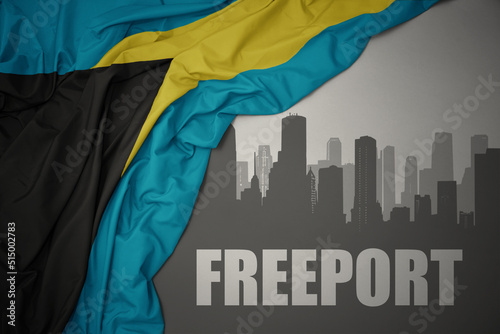 abstract silhouette of the city with text Freeport near waving national flag of bahamas on a gray background. 3D illustration