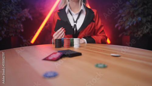 Headless blonde anime school girl hold black poker cards in hand with betting chips out of focus