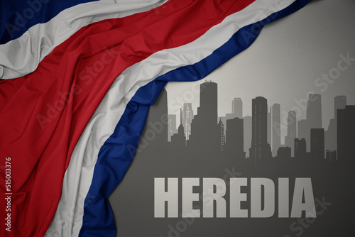 abstract silhouette of the city with text Heredia near waving national flag of costa rica on a gray background. 3D illustration photo