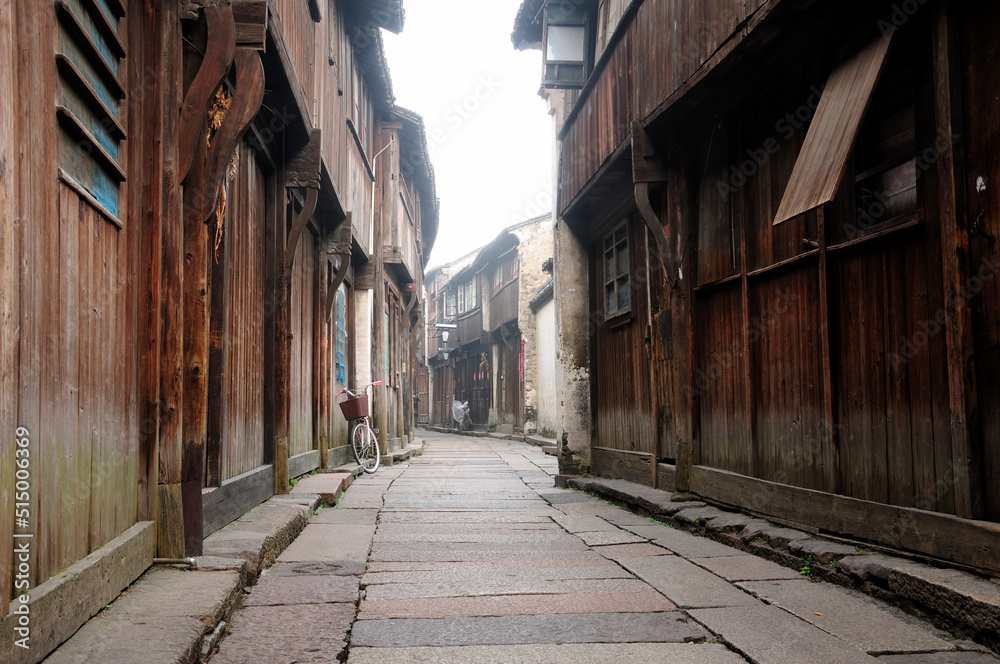 Wooden, weathered buildings lining a narrow walkway in tongxiang wuzhen scenic town east view in Zhejiang province China in the early morning mist.
