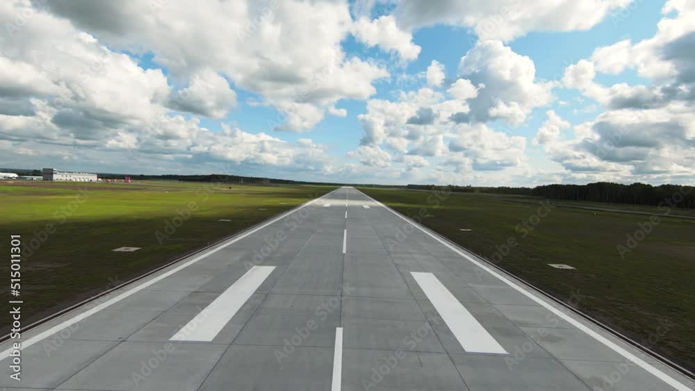 Empty asphalt runway with white markings and light equipment by sides in green field under sky with fluffy clouds Empty asphalt runway with white markings and light equipment by sides in green field under sky with fluffy clouds