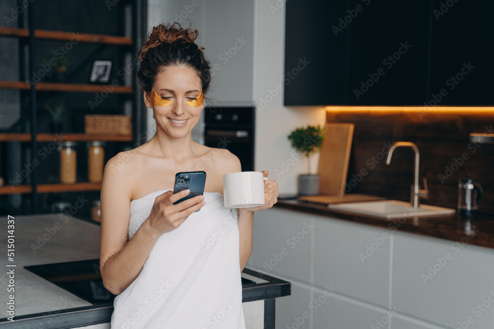 Young woman applies anti wrinkle eye patches and relaxing at home texting on phone.