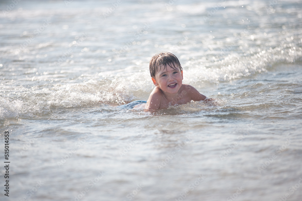 A little boy on the beach, playing with the waves, summer time. Concept of relaxation and a healthy lifestyle