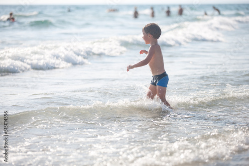 A little boy on the beach, playing with the waves, summer time. Concept of relaxation and a healthy lifestyle © Olivia