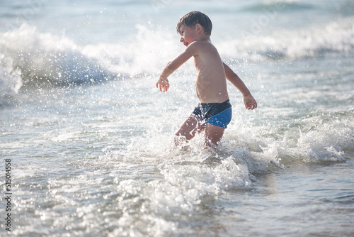 A little boy on the beach, playing with the waves, summer time. Concept of relaxation and a healthy lifestyle