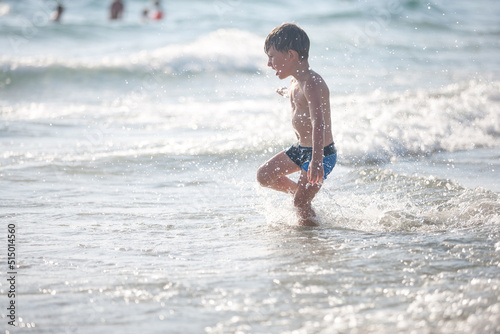 A little boy on the beach, playing with the waves, summer time. Concept of relaxation and a healthy lifestyle