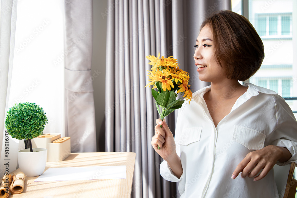 Asian woman in white dress holding sunflowers after hard working in bright interior at home, concept of congratulations on women's day, mother's day or congratulations gift. Asian woman in white dress holding sunflowers after hard working in bright interior at home, concept of congratulations on women's day, mother's day or congratulations gift.