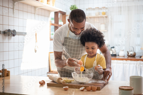 Smiling Black African American Father and little son baking together in kitchen at home