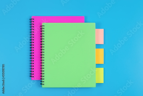 Colourful notebooks and sticky notes arranged on blue background, top view.
