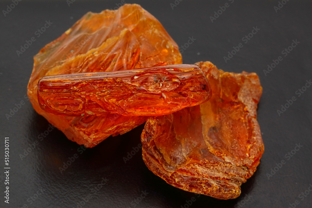 Yellow-red amber on a dark gray background. Natural mineral petrified resin. Material for making jewelry and beads. Copal. Inclusions in resin. Patterns and beautiful crystal texture Yellow-red amber on a dark gray background. Natural mineral petrified resin. Material for making jewelry and beads. Copal. Inclusions in resin. Patterns and beautiful crystal texture