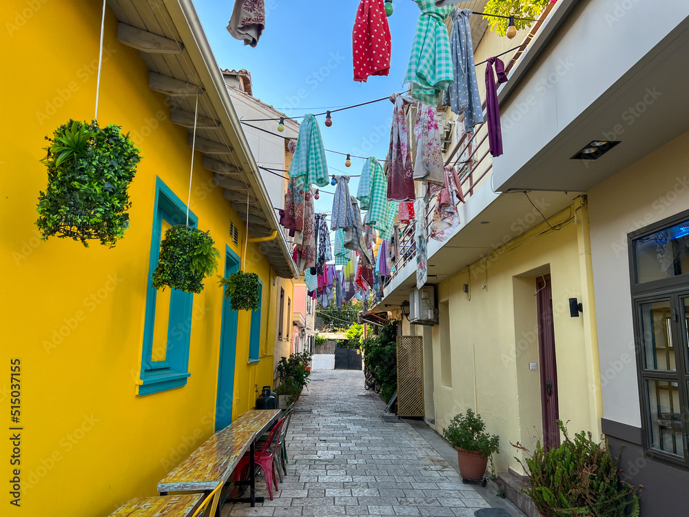 Fototapeta premium Beautiful colored and narrow street in Lefkada Greece covered with colorful ornaments above. Cozy street in the historic center. Brightly colored house walls on the street. Walking around .