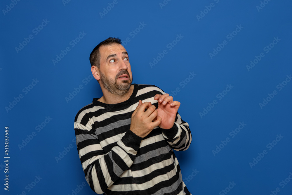 Fototapeta premium Hispanic bearded man tremendously scared by something next to him, copy space. Isolated on blue studio background.