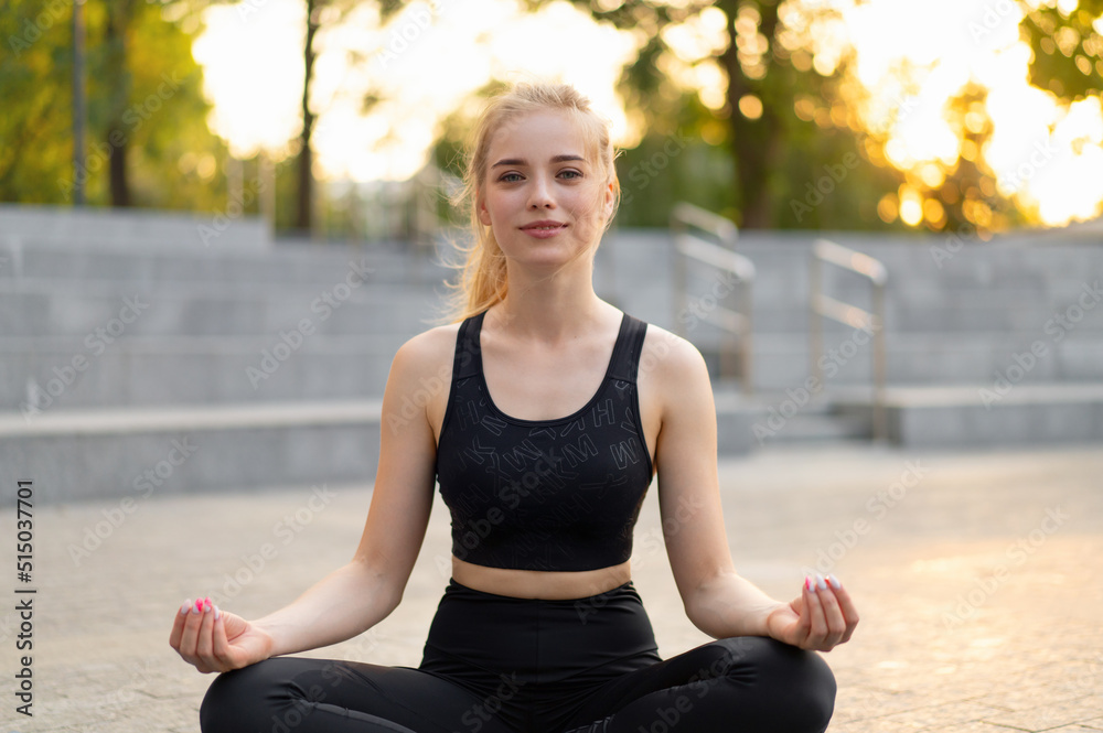 Yoga and Meditation in Modern City Caucasian Woman Relax Lotus Position Sitting Yoga Mat Outdoors Summer Park on Concrete floor Yoga and Meditation in Modern City Caucasian Woman Relax Lotus Position Sitting Yoga Mat Outdoors Summer Park on Concrete floor