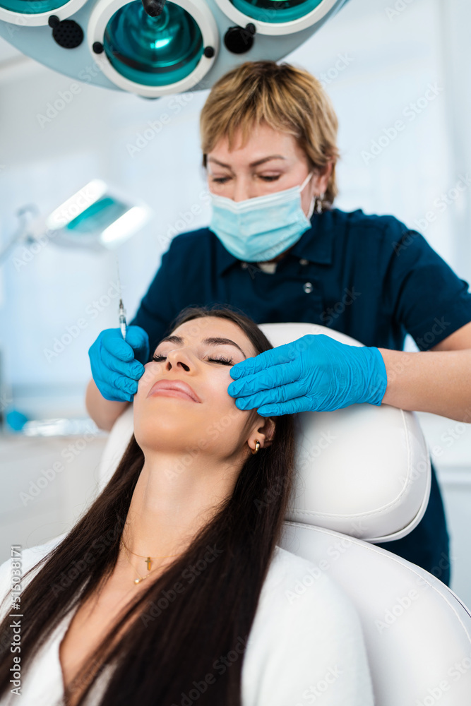 Fototapeta premium Beautician is contouring the woman's cheekbones with hyaluronic acid filler. Hyaluronic acid filler is injected by needle or cannula. Face contouring concept.