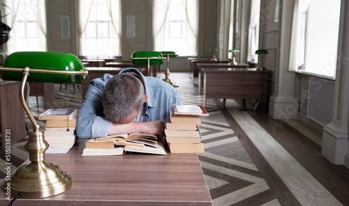 Senior man falls asleep over a textbook, he is sitting at a table that is littered with teaching materials. Portrait of caucasian Senior man working with book in public library. education concept © mars58