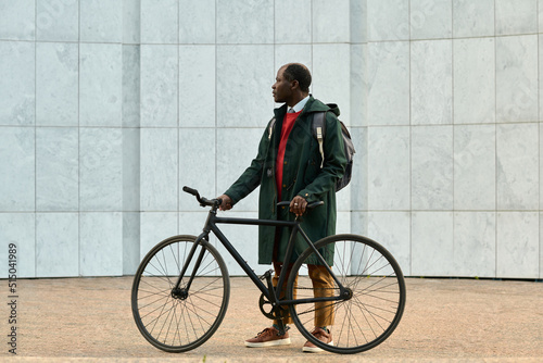 African mature businessman with backpack using his bike to get to the work standing outdoors and looking away