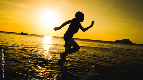 silhouette of boy running on the beach at sunset