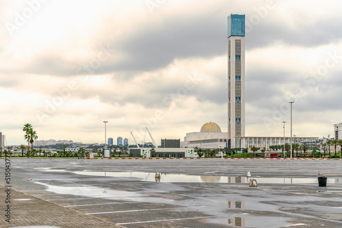 The Great Mosque of Algiers, world's tallest minaret and it's dome seen from Sablettes promenade empty car park with reflection in water on tarmac. Overcast sky with heavy clouds and sunlight diffused