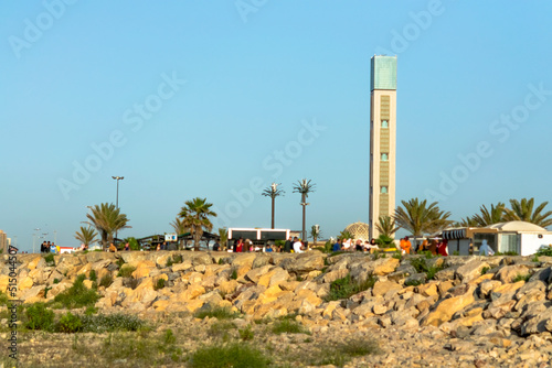 The Great Mosque of Algiers, world's tallest minaret and it's dome seen from Sablettes promenade. Low angle  view of unrecognizable people walking, rocks in foreground, blue clear sky in background. photo