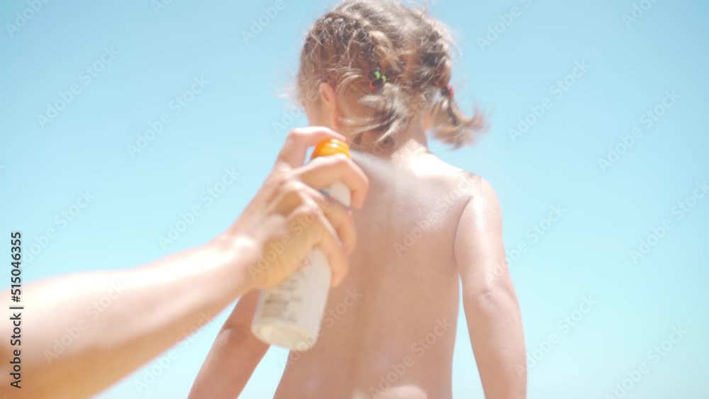 Caring mother apply sunblock to the back and legs her little daughter. Summer vacation sea beach. Caucasian family with one child resting. Sun protection cream. SPF. Happy childhood Positive emotion 