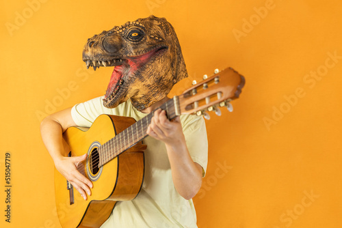 Unrecognizable woman playing guitar wearing dinosaur animal mask isolated on studio orange background