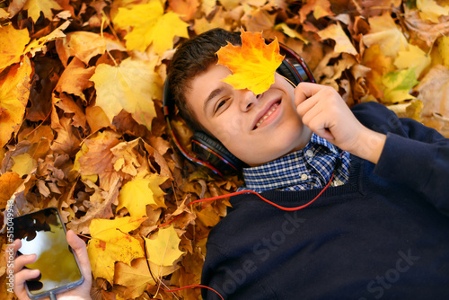 a teenage boy listens to music with headphones  lies on yellow autumn maple leaves  a bright sunny day  beautiful nature in autumn
