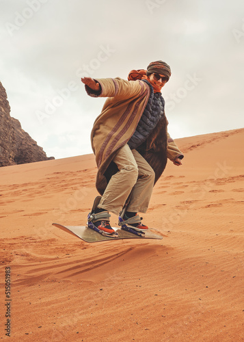 Young woman posing as sand dune surfing wearing bisht - traditional Bedouin coat. Sandsurfing is one of the attractions in Wadi Rum desert photo