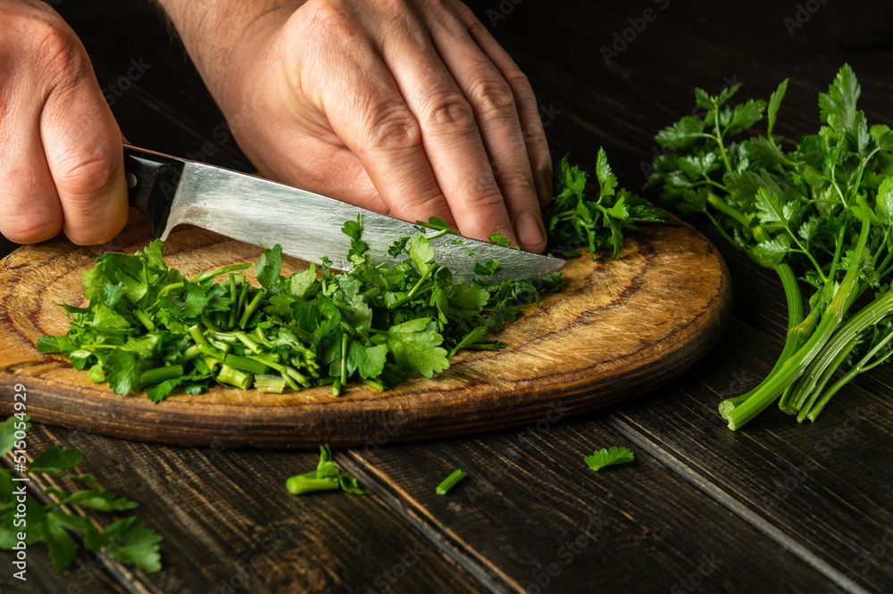 Chef cutting green parsley on a cutting board with a knife for preparing a vegetarian dish. Peasant food.