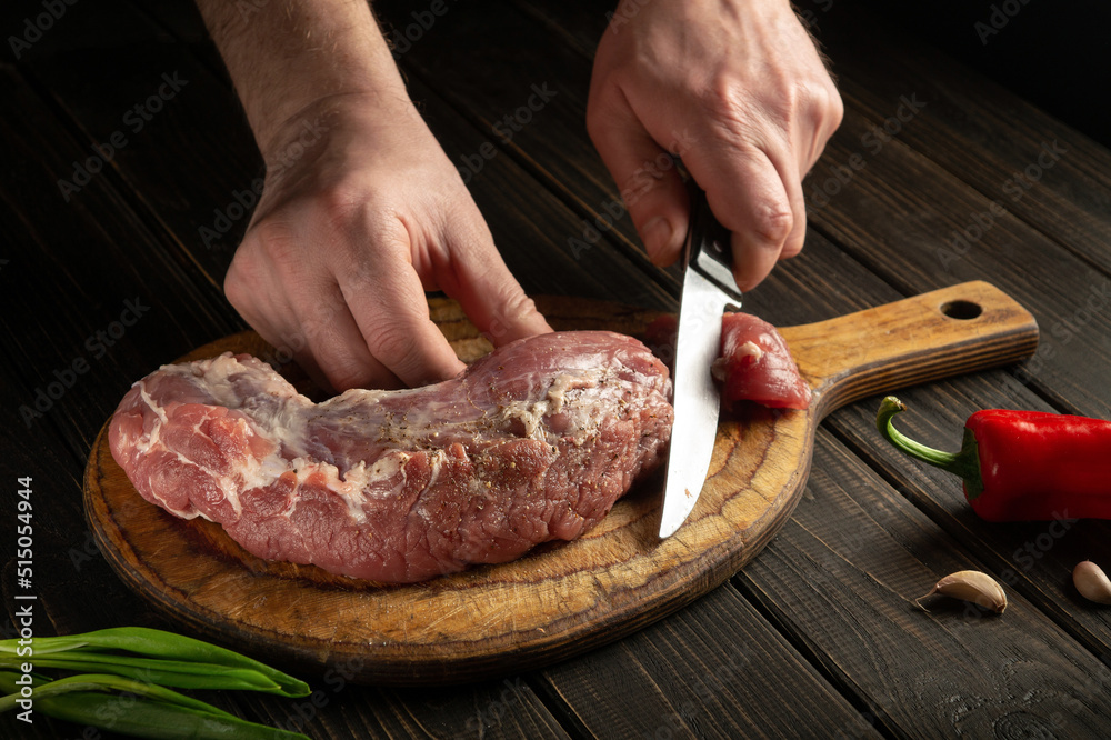 Chef hands cutting raw veal meat on a cutting board before cooking. Peasant foods or home cooking