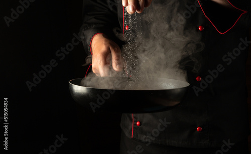 Professional chef adds salt to a hot pan with meat burger cutlets. Free space for hotel menu or recipe on black background