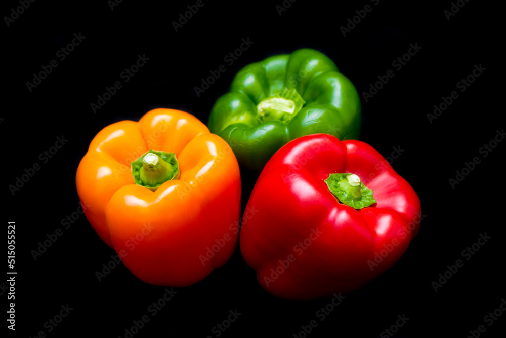 three different colored peppers: red, green and yellow peppers lie on a black background three different colored peppers: red, green and yellow peppers lie on a black background