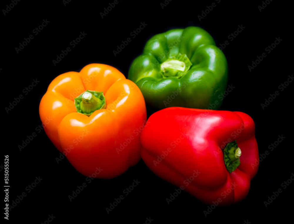 three different colored peppers: red, green and yellow peppers lie on a black background three different colored peppers: red, green and yellow peppers lie on a black background