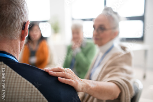 Group of senior people sitting in circle during therapy session, woman consoling depressed man.